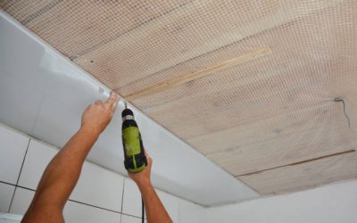 Contractor installing white PVC Ceiling Boards with screw gun in the bathroom